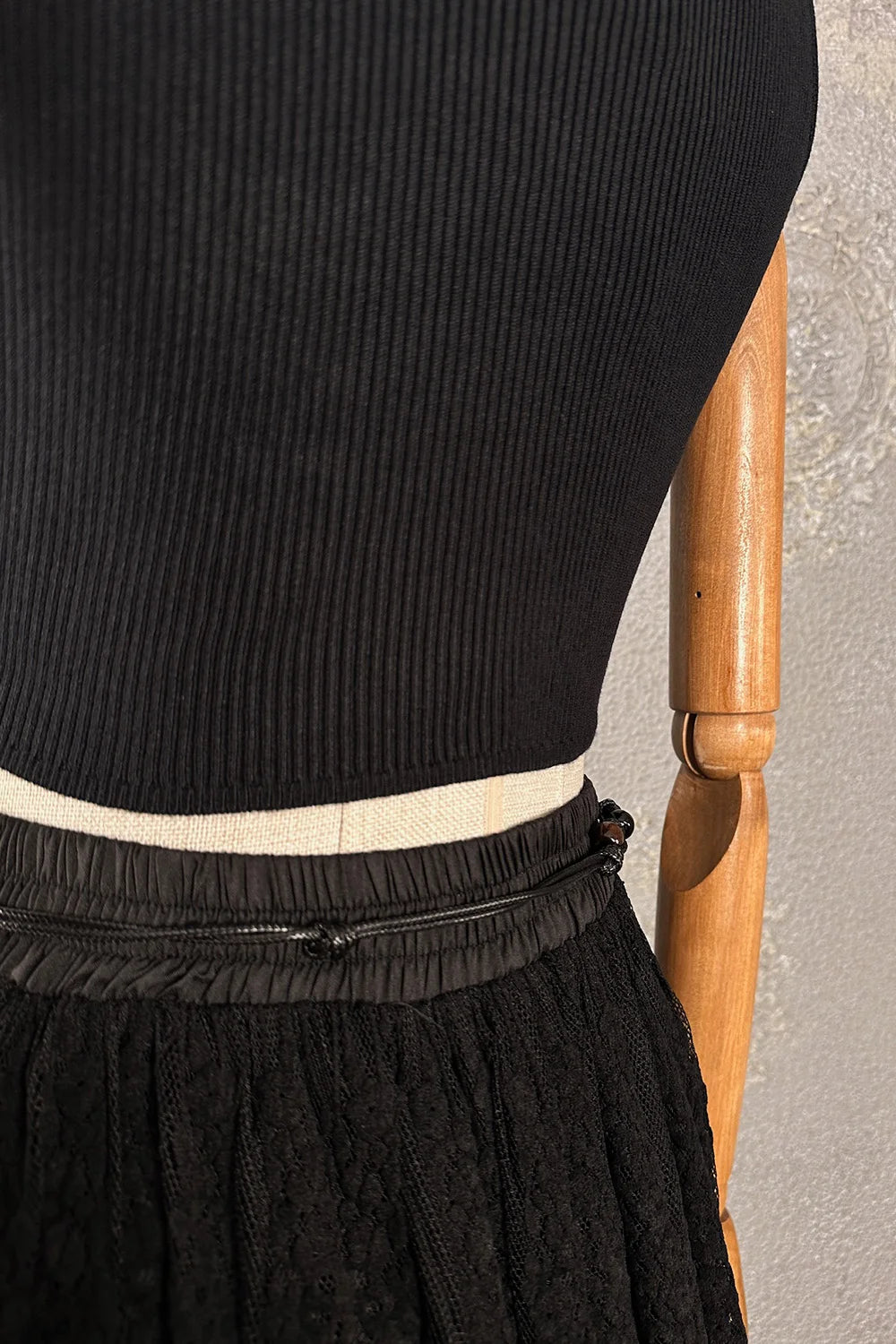 Siyah crop triko bluz, ribli kumaş, elastik bel detaylı, kadın giyim, yandan görünüm, ahşap askı üzerinde