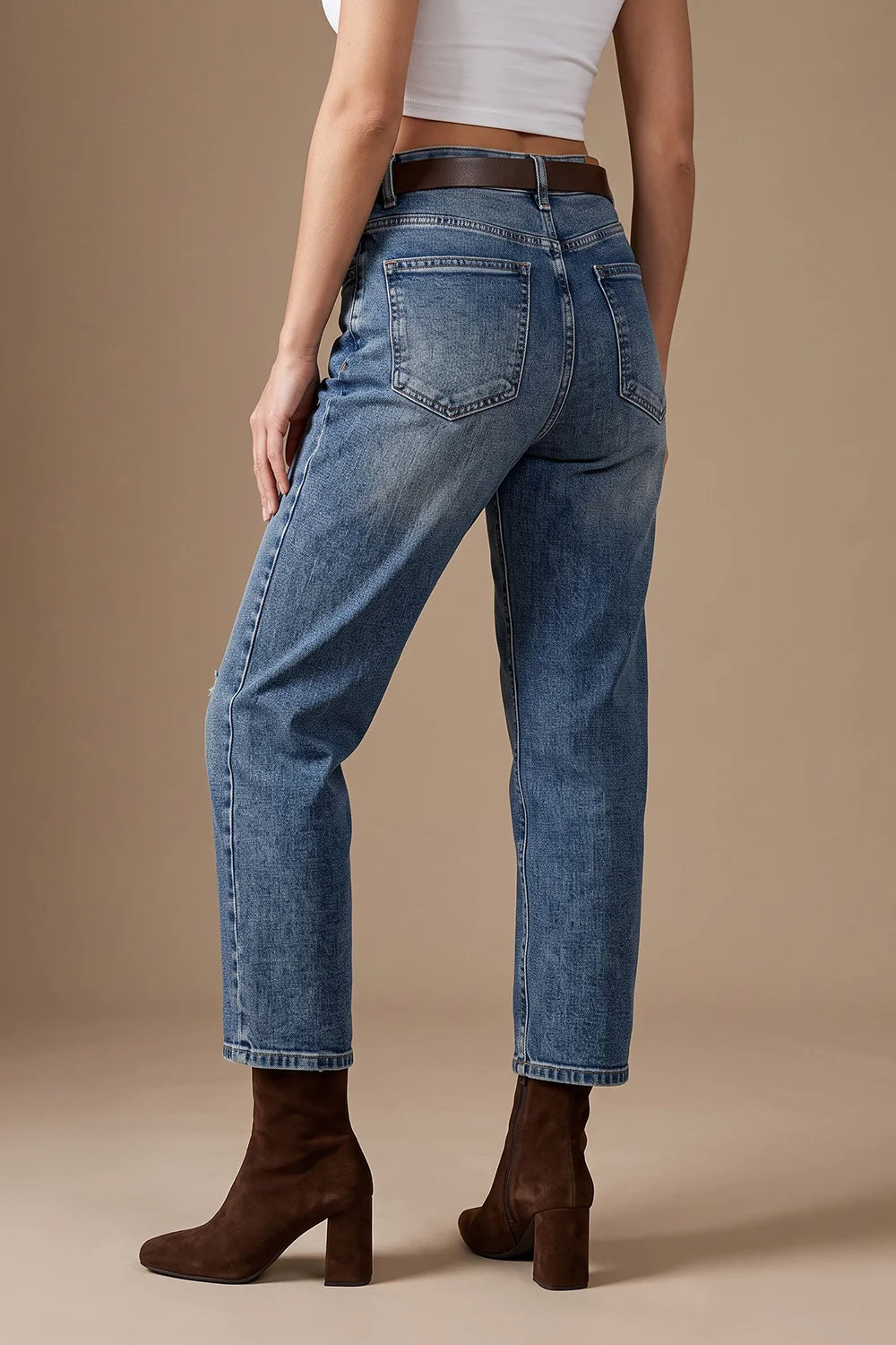 Taşlamalı mom jean, açık mavi denim, yüksek bel, düz kesim, kahverengi kemer ve çizme ile yandan görünüm.