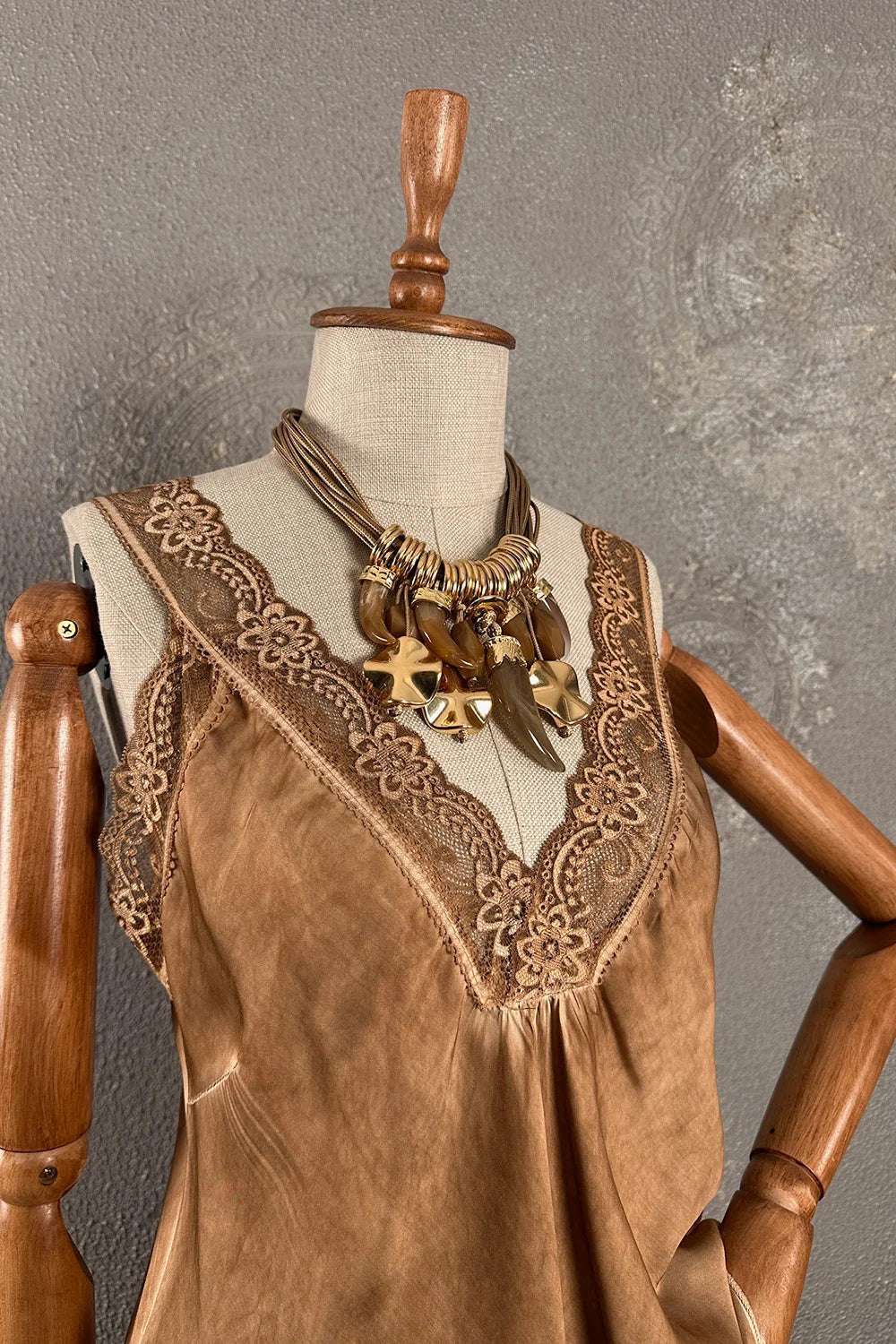 Bej saten kadın bluz, dantel yaka detaylı, kolsuz kesim, altın aksesuar ile stilize, önden görünüm.