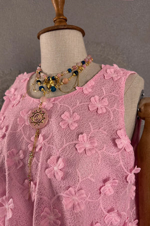 Pembe çiçekli dantel elbise, kolsuz kesim, detaylı boncuk ve sun kolye aksesuarı, ön görünüm.