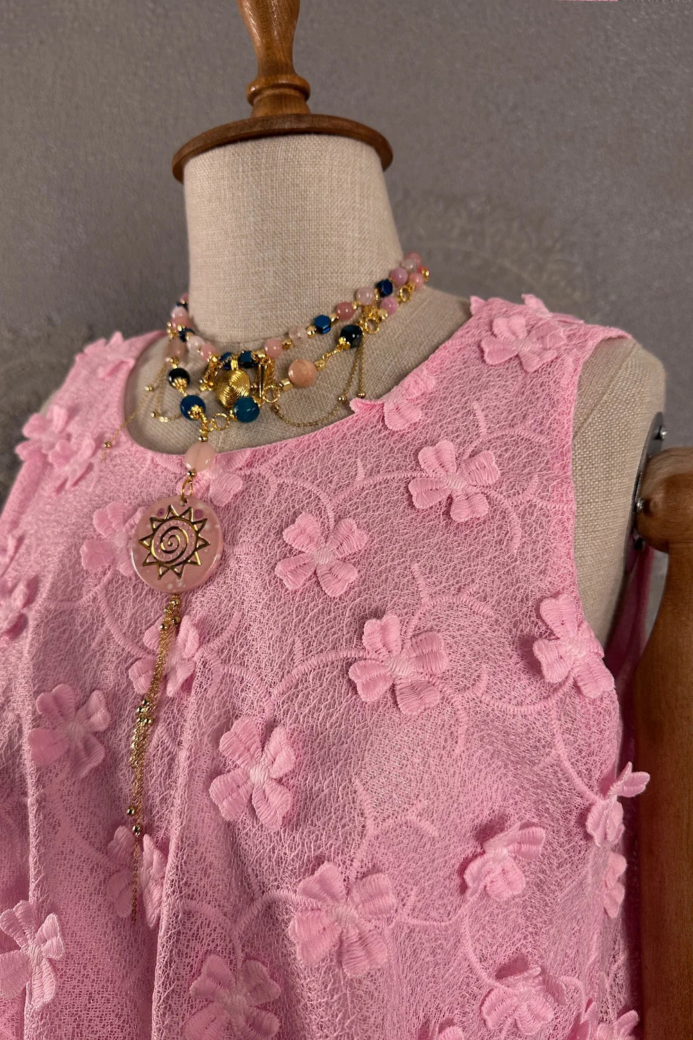 Pembe çiçekli dantel elbise, kolsuz kesim, detaylı boncuk ve sun kolye aksesuarı, ön görünüm.